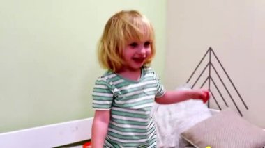 Neşeli genç bir çocuk, parlak ve rahat bir mekanda oynuyor. Bebek kıkırdıyor ve enerjik bir şekilde hareket ediyor, oyun zamanı heyecanı ve merakı gösteriyor.