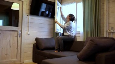 Konforlu bir kamaranın oturma odasında perdeleri indiren bir kadın görülüyor. Sıcak uzay, topraksı tonlar ve doğal ışık barındırarak rahatlatıcı bir atmosfer yaratıyor..