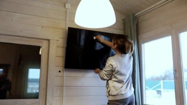 Parlak ve havadar bir odada bir kadın televizyon ekranını temizliyor. Ahşap duvarlar ve büyük pencereler sıcak ve davetkar bir atmosfer olduğunu gösteriyor..