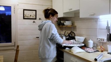 Bir insan sıcak bir mutfakta ustalıkla yemek hazırlamakla meşgul. Oda ahşap aksanlarla tasarlandı ve rahat atmosfer yemek pişirme deneyimini arttırıyor..