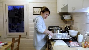 Bir insan sıcak, davetkar bir mutfakta lezzetli bir yemek hazırlar. Doğal ışık pencereden süzülerek, çalışırlarken pişirme sürecini vurgular..