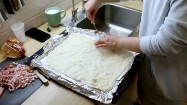 Doğal ışıkla dolu sıcak bir mutfakta, insan lezzetli bir yemek için hamur toplar, desen oluşturmak için çatalı dikkatlice kullanır. Et gibi malzemeler yakınlarda, yemek pişirme sürecini vurguluyorlar..
