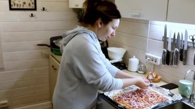 Bir kadın sıcak bir mutfakta ev yapımı pizza hazırlar, hamur yoğurur ve malzemeler ekler. Mekan büyüleyici, yemek aletleri ve rahatlatıcı bir ortam var..