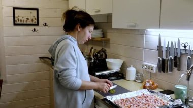 Bir kadın sıcak bir mutfakta sebze doğramakla meşgul. Etrafı taze malzemelerle çevriliyken görevine odaklanıyor ve besleyici bir yemek yapıyor. Hava sıcak ve davetkar..