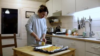 Bir kadın iyi aydınlatılmış bir mutfakta renkli bir yemek hazırlar, malzemeleri doğrar ve pişirme tepsisine yerleştirir. Akşam ortamı yemek pişirme deneyimini güçlendirir..