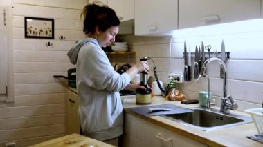 Bir insan mutfak tezgahında durur ve malzemeleri küçük bir aletle harmanlar. Mekan sıcak bir şekilde ışıklandırılmış ve davetkar bir atmosfer yaratacak çeşitli çatal bıçaklara sahiptir..