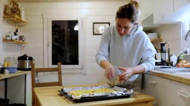 Sıcak bir mutfakta, bir insan yemek tepsisinin üzerine malzemeleri dikkatlice serper. Akşam ışığında yemek pişirildikçe atmosfer rahatlıyor..