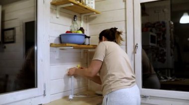 Bir kadın öğleden sonrasını mutfağını temizleyerek ve düzenleyerek, rafları düzgünce düzenleyerek ve çalışma alanıyla ilgilenerek geçirir. Hava sıcak ve davetkar..