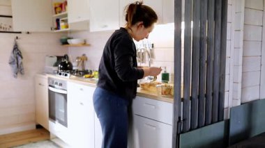 Bir kadın sıcak ve davetkar bir mutfakta yemek pişirirken tezgahtaki malzemeleri düzenliyor. Doğal ışık boşluğu suyla doldurur, sade atmosferi güçlendirir..