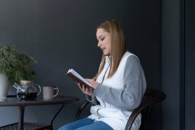 Genç bir kadın rahat rahat bir köşede oturuyor, yanında bir fincan kahveyle kitap okuyor. Minimalist bir dekorla çevrili sakin bir öğleden sonranın tadını çıkarıyor..