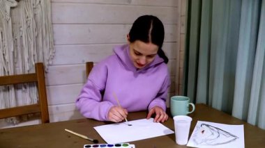 Genç bir sanatçı evde yaratıcı bir resim seansından zevk alır, masadaki araç gereçler ve malzemelerle, rahat bir atmosferle çevrili iken sanatsal çalışmalarına odaklanır..