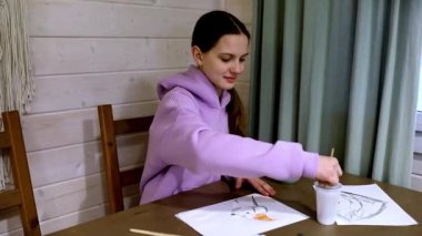 Bir kız, rahat ve sıcak bir mekanda, ahşap bir masada resim yapmaya dalmış. Bir içkiyi yudumlarken sanat yaratmak için fırça ve suluboya kullanır..