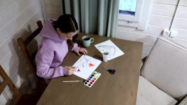 Bir insan, suluboya sanatı yaratmaya dalmış, ahşap bir masada rahatlatıcı bir resim anından zevk alır. Kapalı alan atmosferi bir fincan çay ve sanat malzemesi içeriyor, ilham verici..