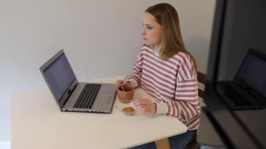 Genç bir kadın laptopuna odaklanmış basit bir masada oturur ve küçük bir atıştırmanın tadını çıkarır. Parlak oda çalışmak ya da çalışmak için davetkar bir ortam yaratır..