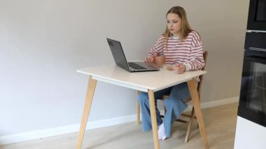 Bir kadın basit bir masada oturur, bilgisayarına odaklanırken kahvesini yudumlar. Parlak oda minimalist bir tasarım içeriyor, rahatlatıcı bir çalışma alanı yaratıyor..