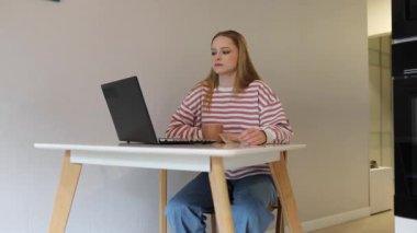 Genç bir kadın şık evinde masa başında oturuyor, dizüstü bilgisayarıyla meşgul. Hafif bir ikramla besleniyor. Hoş bir ortamda verimlilik ve rahatlama karışımını vurguluyor..