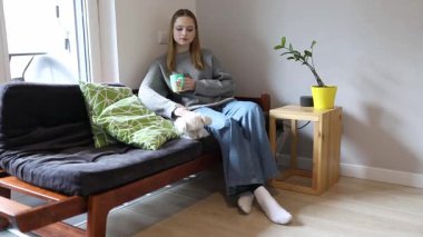 Küçük bir köpek yanında dinlenirken bir kadın rahat bir oturma odasında kahvesinin tadını çıkarıyor. Modern dekor uzaya sıcak, davetkar bir atmosfer ekler..