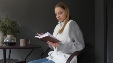 Genç bir kadın terasta rahat bir şekilde oturur, sıcak bir fincan kahve ve huzurlu bir atmosferin tadını çıkarırken kendini kitabına kaptırmıştır. Ortalık sakin ve davetkar..