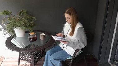 Genç bir kadın balkonunda rahatça oturur, kahvesini yudumlar ve bir kitaba dalmıştır. Sakin atmosfer, rahatlama ve odaklanmayla dolu mükemmel bir sabahı davet ediyor..