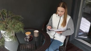 Genç bir kadın gölgeli bir verandada rahatlar, kahve içerken kitap okur. Ortalık sakin ve davetkar. Etrafı yeşil ve rahat mobilyalarla çevrili..