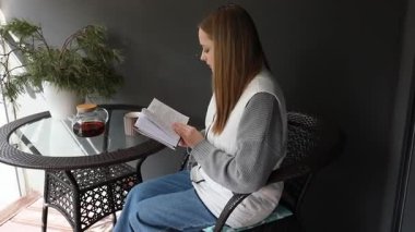 Genç bir kadın balkonunda sakin bir öğleden sonra geçirir, kitabına dalmışken sıcak bir içki yudumlar. Konforlu sette bir saksı bitkisi ve bir bardak çay bulunuyor..