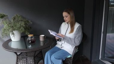 Genç bir kadın günlük tutarken kahvenin tadını çıkarırken balkonda huzurlu bir sabah için yerleş. Sakin atmosfer yansımayı ve sakinliği davet eder..