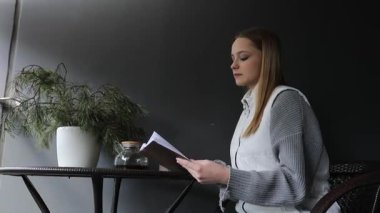 Genç bir kadın, rahat bir kafede küçük bir masada oturur. Etrafı bitkilerle çevriliyken kitap okur. Barışçıl ortam rahatlamayı ve odaklanmayı teşvik eder..