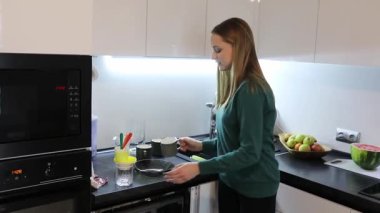 Genç bir kadın yenileyici bir içecek yaparak çağdaş bir mutfakta yeteneklerini sergiliyor. Gülümserken mutfak aletleri ve taze malzemelerle meşgul oluyor..