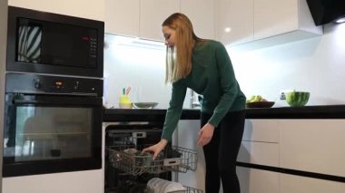 Gösterişli, modern bir mutfakta akşam yemeği hazırlıklarından sonra bulaşıkları bulaşık makinesinde yıkar. Parlak ışıklar mekanı aydınlatır, şık dolabı ve tezgahı aydınlatır..