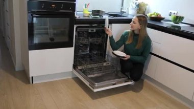 Bir kadın, çağdaş bir mutfakta dururken bulaşık makinesinde temiz bulaşıklar organize eder. Sabah ışığı boşluğu dolduruyor, fonksiyonel tasarımı vurguluyor.