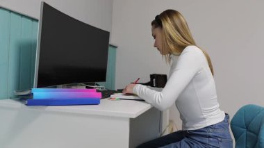 Odaklanmış bir öğrenci masa başında faaliyetler üzerine çalışır. Parlak ışıklandırma, notlar alırken ve materyalleri incelerken, kendini öğrenmeye adadıkça, canlı bir atmosfer ekler..