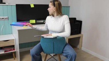 Genç bir kadın çalışmalarına renkli yapışkan notlar ve bir dizüstü bilgisayarla çevrili bir ofis ortamında odaklanıyor..