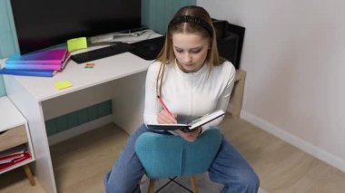 İyi ışıklandırılmış bir odada, bir kız sandalyeye oturur, derslerine odaklanır. Renkli kırtasiye malzemeleri ve bilgisayar düzeneği ile çevrili iken bir deftere yazarak öğrenmeye olan bağlılığını gösteriyor..