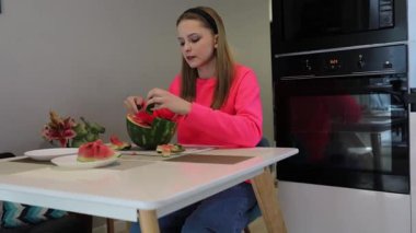 Parlak bir mutfakta, bir insan dikkatlice karpuz parçalarını toplar ve ferahlatıcı bir atıştırmalık oluşturur. Çalışırken canlı renkleri ve tatlı aromayı severler..