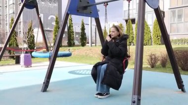 Genç bir kız, güzel tasarlanmış bir oyun alanıyla çevrili bir salıncakta oturuyor. Dışarıda temiz havanın tadını çıkarırken güneş ışıl ışıl parlıyor..