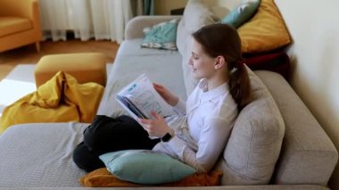 Genç bir kadın sıcak bir oturma odasındaki kanepede rahat bir şekilde oturur ve defterini okumaya dalmıştır. Yastıklar ve battaniyeler rahat atmosfere eklenir.