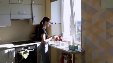 Modern bir mutfağın penceresinde duran bir insan, güneş ışığının tadını çıkarırken bir kâsede malzemeleri karıştırıyor ve lezzetli bir yemek için hazırlanıyor..