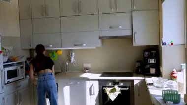 Parlak bir mutfakta, bir kız yemek hazırlamakla meşgul. Çalışma alanını düzenlemeye ve temizlemeye odaklanıyor. Mutfak becerilerini ve detaylara olan ilgisini gösteriyor..