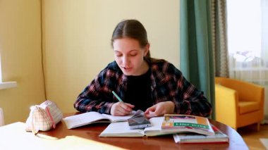 Genç bir kadın, sıcak bir odadaki ahşap bir masada derslerine odaklanıyor. Etrafı kitaplarla çevriliyken ve tarih dersine dalmış akıllı bir telefonla notlar yazıyor..