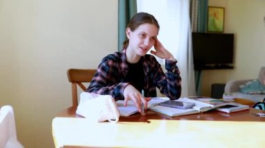 Genç bir kadın çalışmalarına ahşap bir masada odaklanmış, etrafı kitap ve notlarla çevrili sıcak bir odada. Düşüncelere dalmış, çeşitli öğrenme materyallerini dengeliyor..