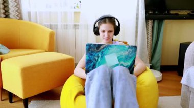 Genç bir öğrenci laptopuna odaklanmış, kulaklık takmış bir şekilde fasulye çuvalının üzerine rahatça oturur. Renkli odanın parlak ve davetkar bir havası var. Çalışmak için mükemmel..