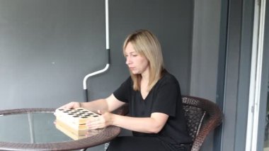 Bu video terasa satranç tahtası kuran bir kadını gösteriyor. Bir sandalyede oturuyor ve teras bir yerleşim bölgesinde gibi görünüyor..