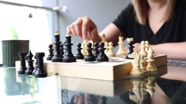 Bir kadın güneşli terasta satranç oynuyor. Bir sonraki hamlesini planlarken tahtaya odaklanmış durumda. Kamera kadınların ellerini ve satranç taşlarını yakalar..