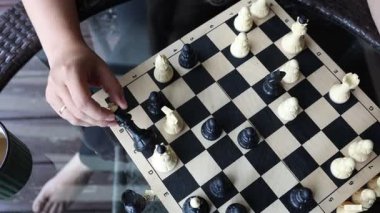 Bir kadın terasta oturur ve satranç oynar. Satranç tahtası cam bir masaya kurulmuş ve kadın bir sonraki hamlesini dikkatlice düşünüyor. Güneş ışıl ışıl parlıyor, sıcak bir ışık saçıyor.