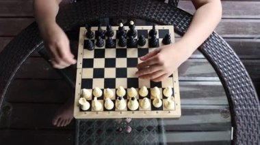 Bir kadın terasta bir masada oturur ve satranç oynar. Yaz öğleden sonranın tadını çıkarırken tahtaya hamle yapar..