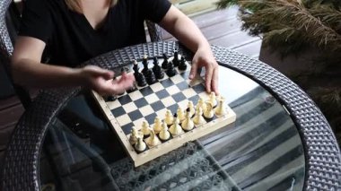 Bir kadın gün içinde terasta satranç oynuyor. Satranç tahtası cam tepeli bir masaya kurulmuş ve kadın siyah bir gömlek giyiyor. Bir sonraki hamlesine konsantre oluyor gibi görünüyor.