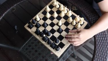 Bir kadın terasta oturur ve cam bir masada satranç oynar. Satranç tahtası önüne serilmiş ve o da eliyle bir parça hareket ettiriyor. Güneş ışıl ışıl parlıyor ve gökyüzü...
