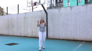 Bu video açık hava sahasında basketbol oynayan beyaz bir kadını gösteriyor. Beyaz pantolon ve gri bir atlet giyiyor ve oyunundan hoşlanıyor gibi görünüyor. Sarayın etrafı sarıldı.