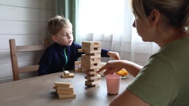 Bir anne ve küçük oğlu mutfak masalarında klasik masa oyunu Jenga oynuyorlar. Çocuk abur cubur yerken annesi kulenin bloklarını dikkatlice kaldırıyor..
