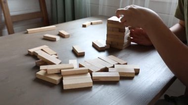 Bir anne ve oğlu evlerinde Jenga oynuyorlar. Çocuk, annesi dikkatle izlerken kuleden bir blok çekiyor..